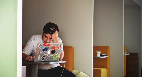 man crouched over laptop with hand in head doing wordpress maintainance and being frustrated by errors