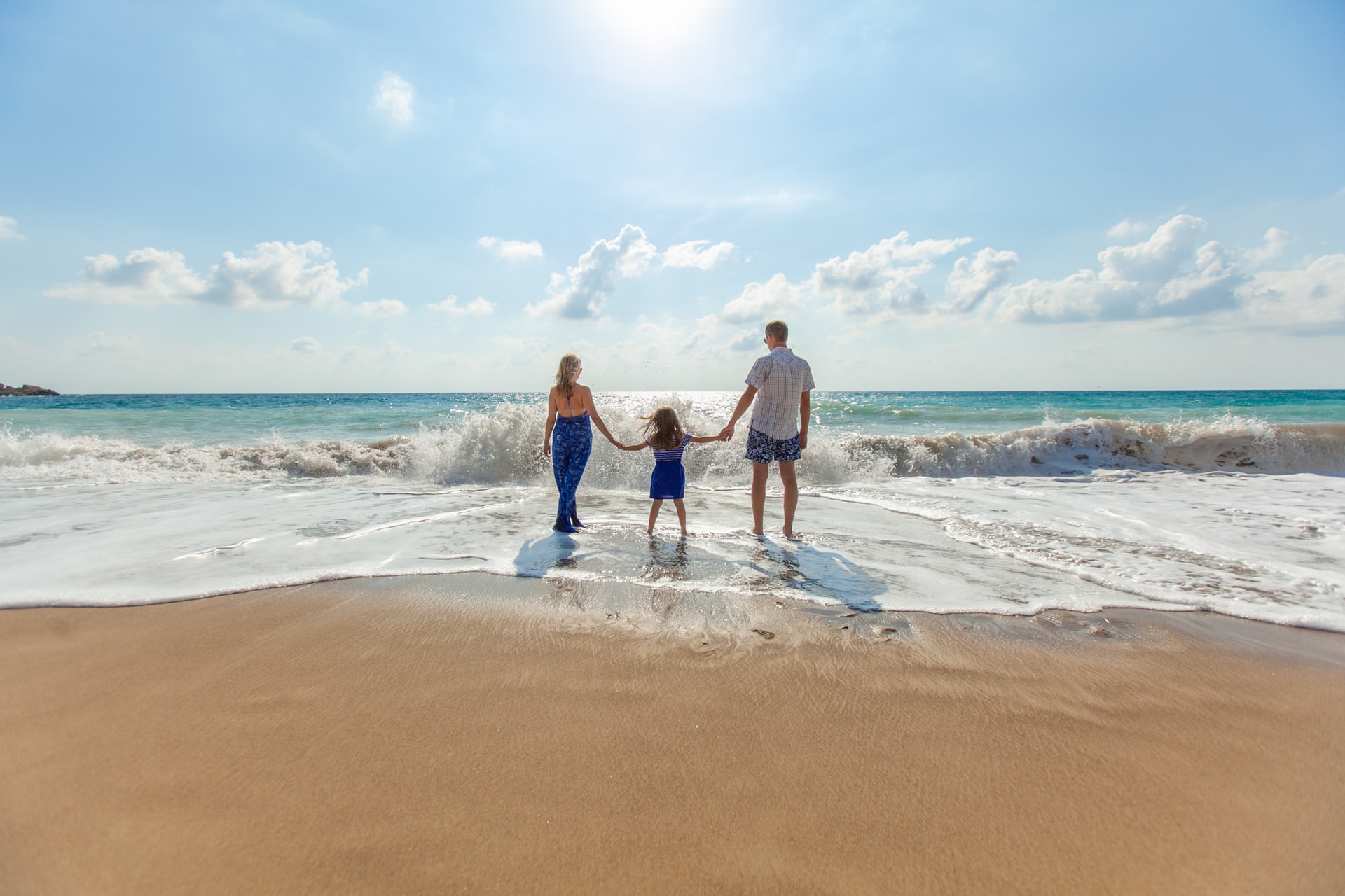 man woman and child wlking out to sea holding hands